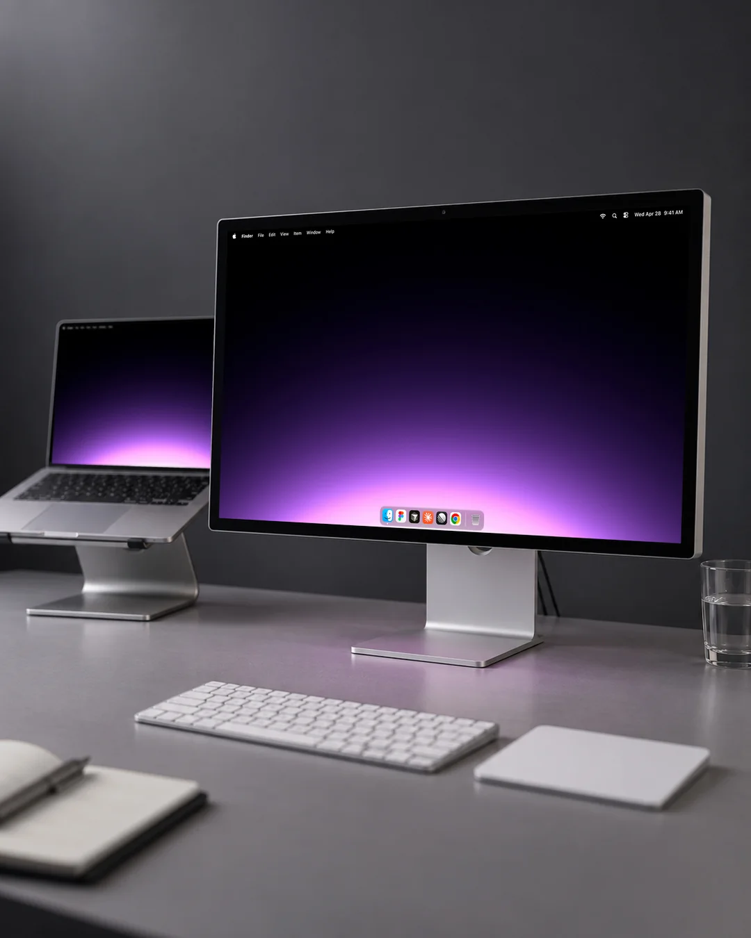 A Gradient wallpaper on a desktop display beside a laptop on a stand, a violet glow rising out of black
