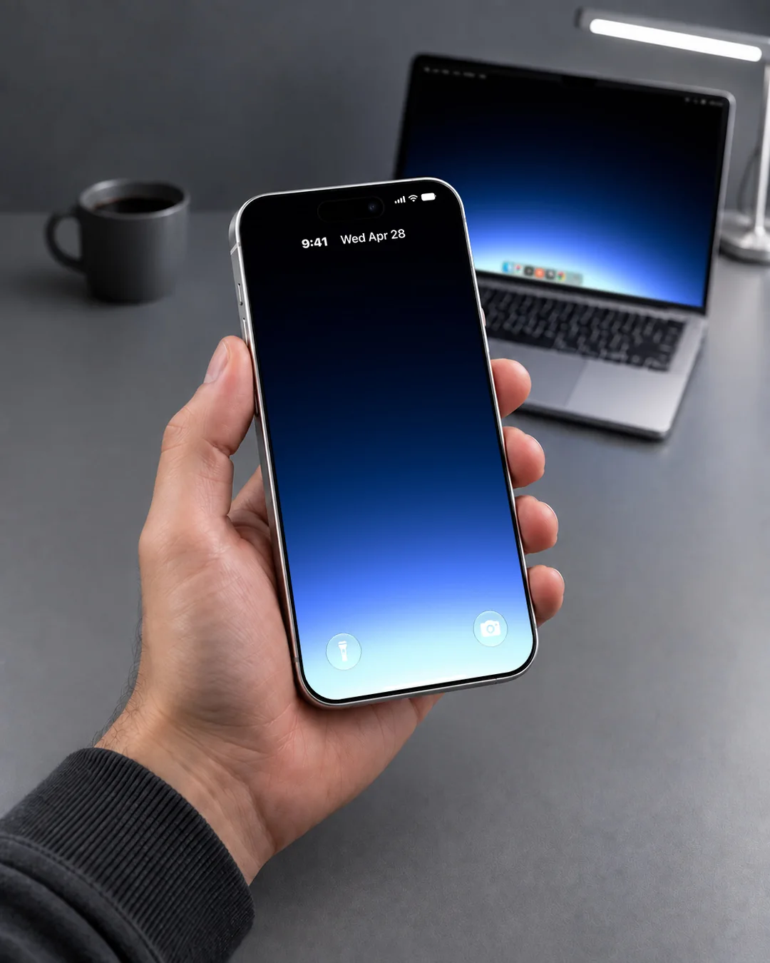 A Gradient wallpaper on a phone held in front of an open laptop, both screens a blue glow on black